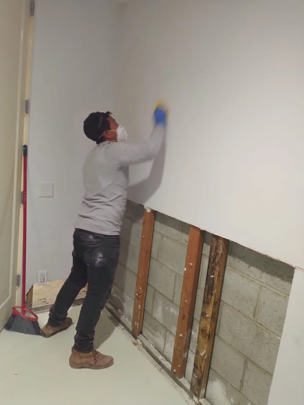 Technician in a respirator and gloves pulling drywall during a flood cut, exposing the concrete block wall behind.