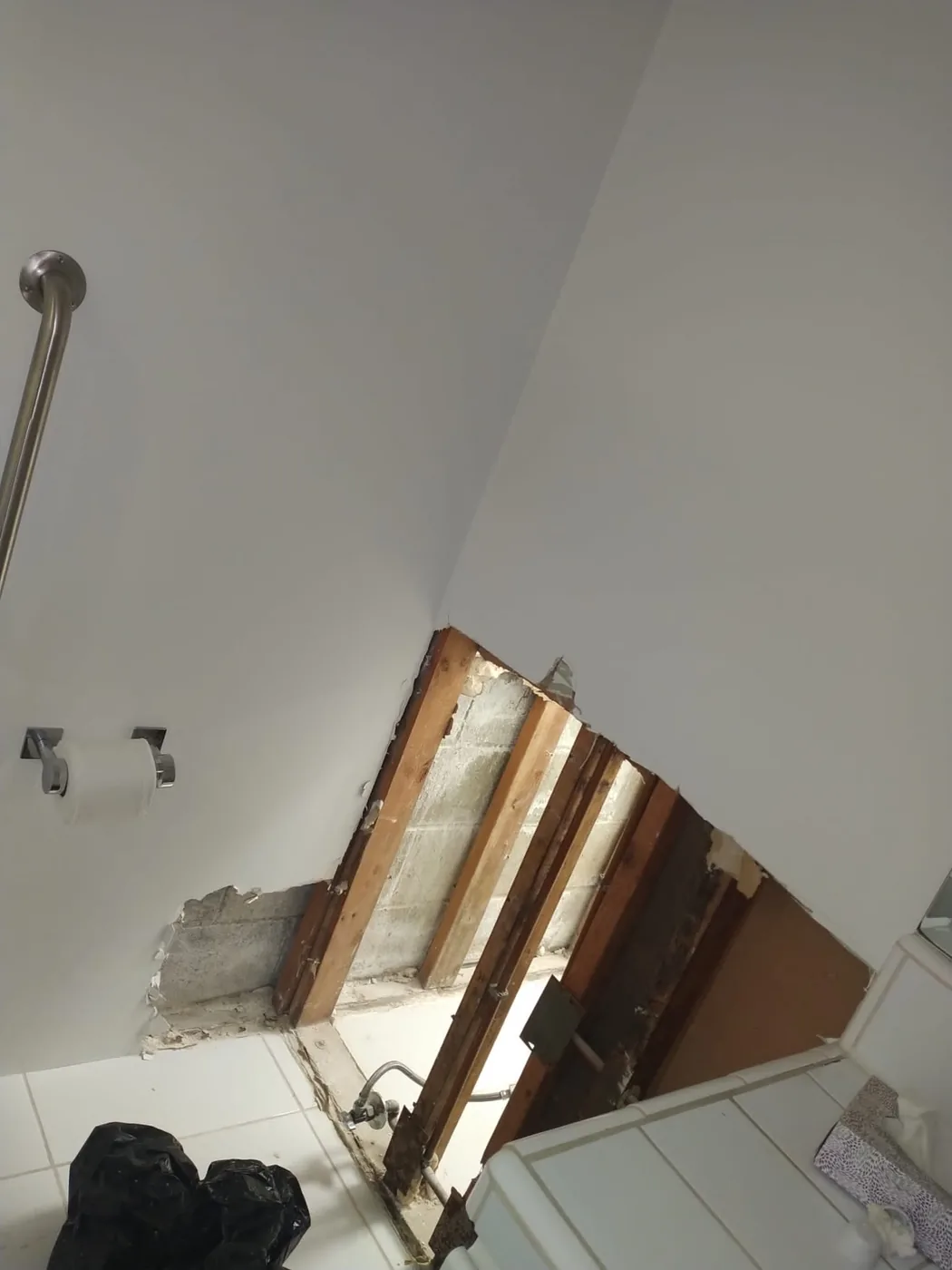 Bathroom drywall removed behind the toilet, exposing concrete block, wood furring strips, and moisture staining.